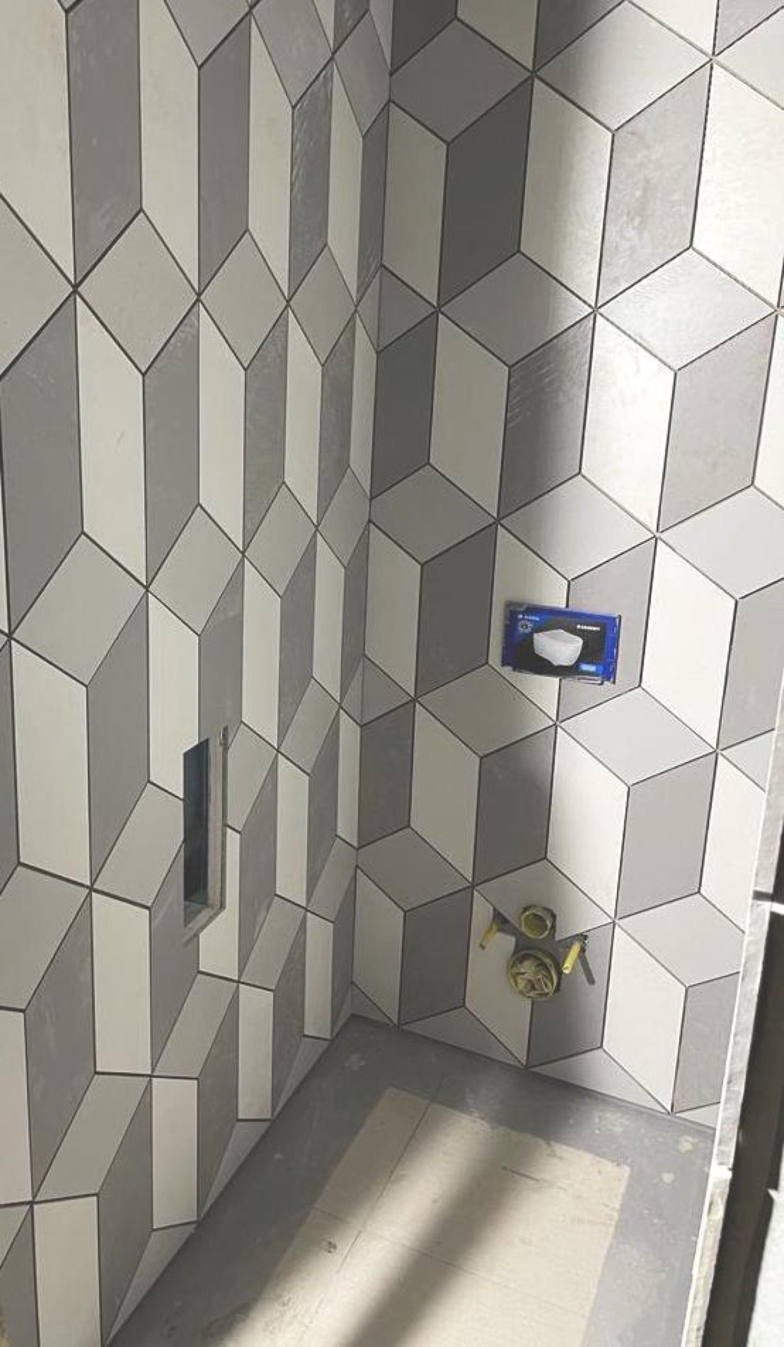 camt-badwand-im-rohbau-mit-grau-weissen-rautenfliesen-im-kubusmuster-mit-wc-vorwand-und-wandnische