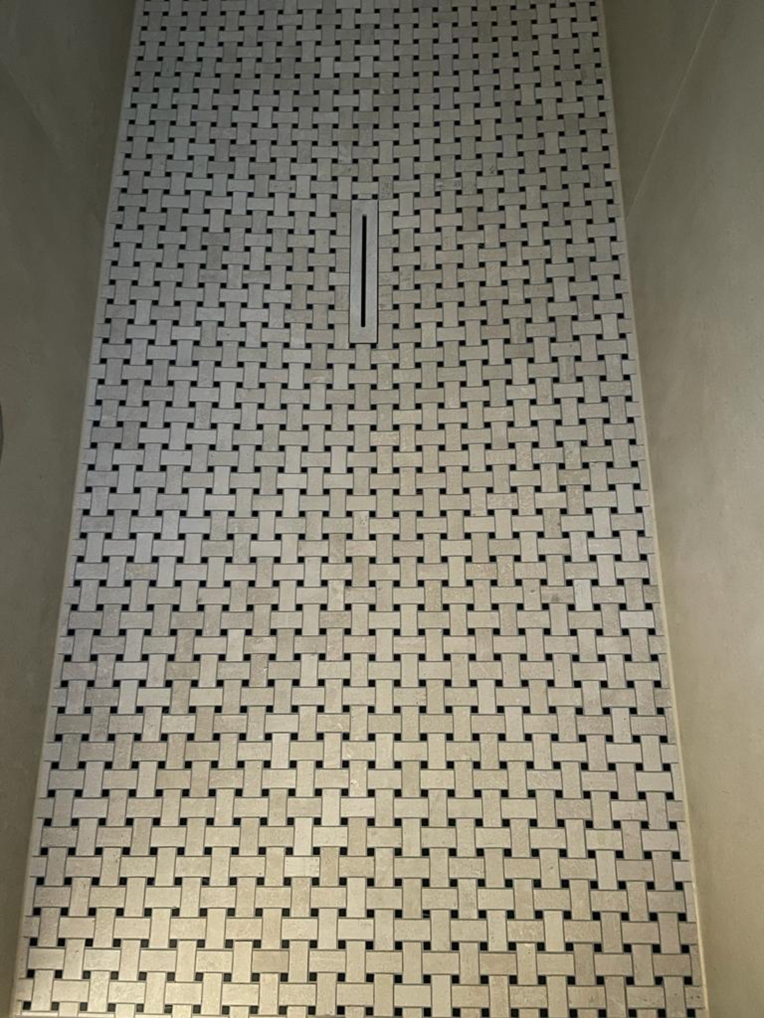 Fertig verlegter Duschboden mit Korbgeflecht-Mosaik aus hellen Steinstreifen und schmaler Ablaufrinne