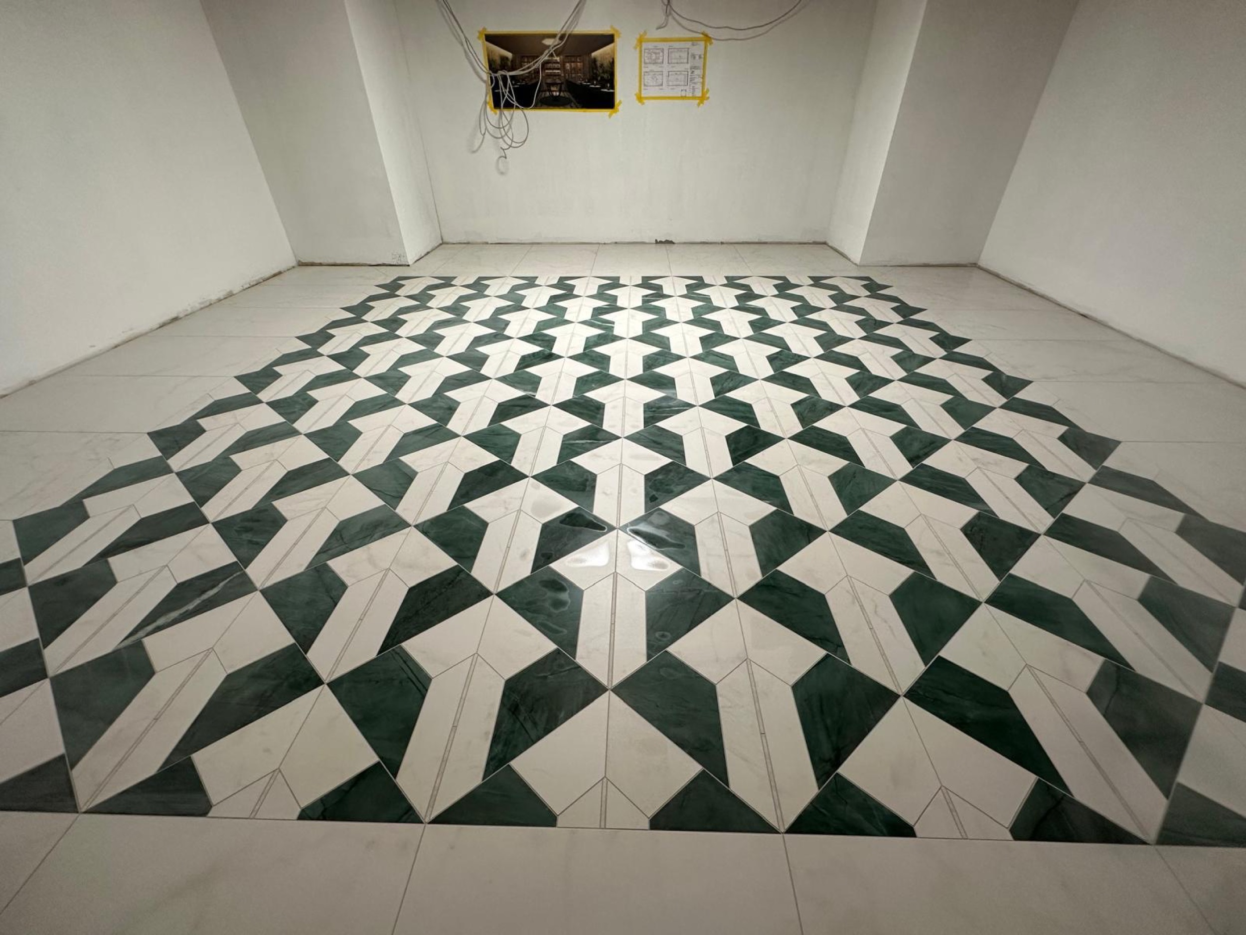 camt gruen weisses bodenmuster in quadratischer flaeche in weiss getuenchtem raum schraeg von vorn fotografiert mit kabeln und plaenen an der wand