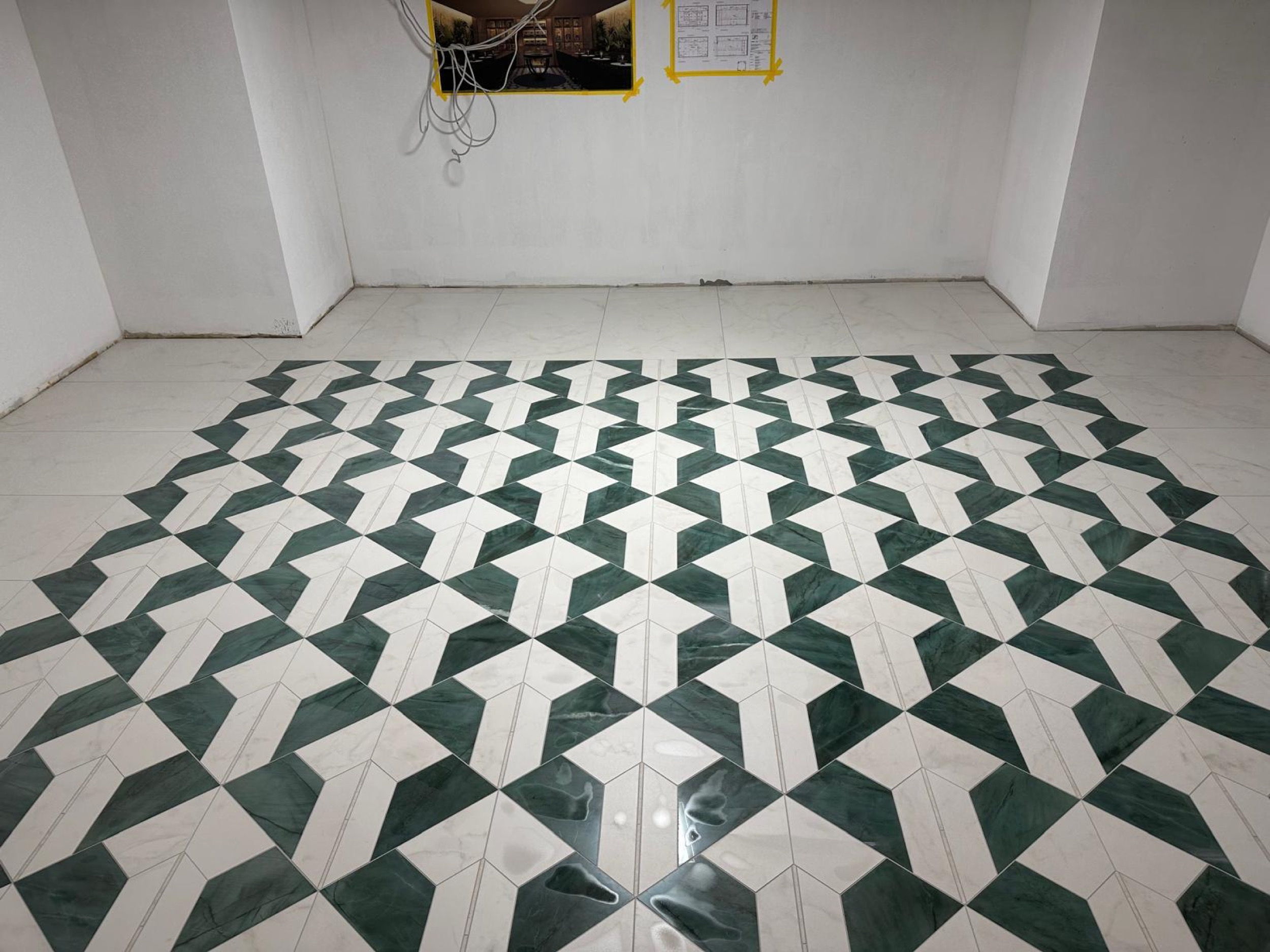 camt gruen weisses bodenmuster in quadratischer flaeche mit hellem plattenrand in weiss getuenchtem raum mit kabeln und plaenen an der wand frontal
