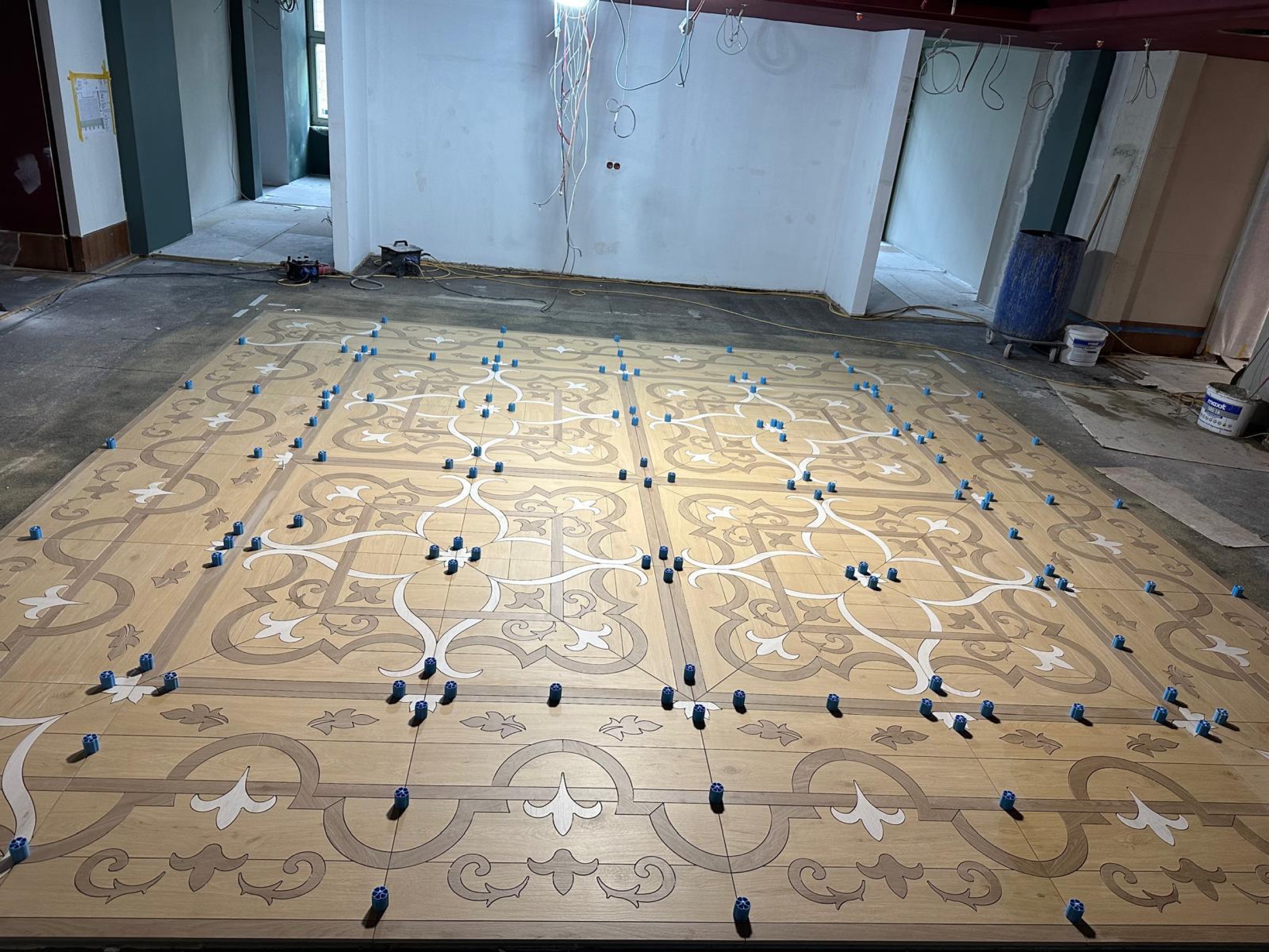camt ornamentboden in holzoptik mit blauen nivellierklammern frontal vor weisser wand in baustelle