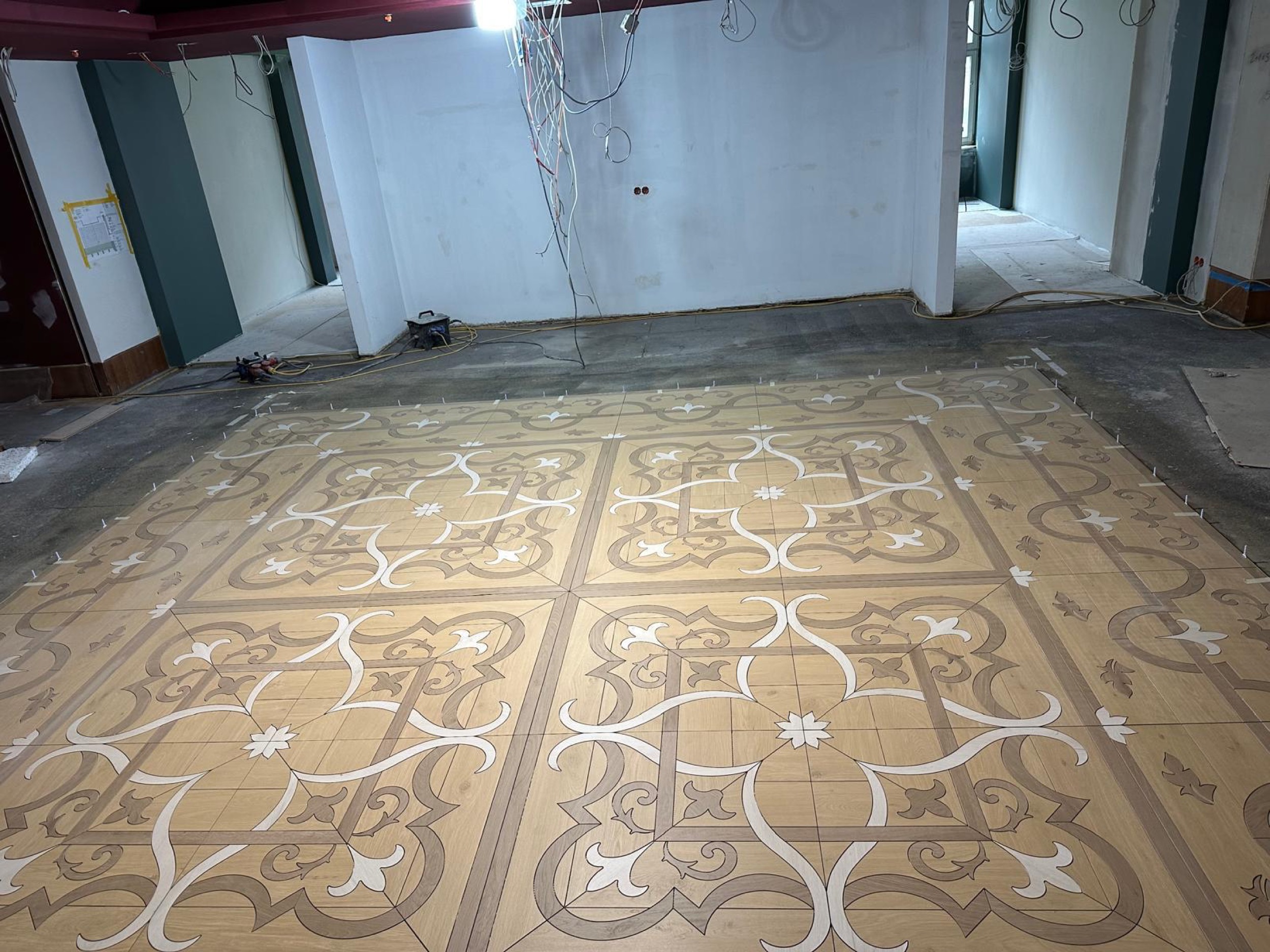camt ornamentboden in holzoptik naeher mit weissen lilienmotiven und verspielten ranken vor weisser trockenbauwand