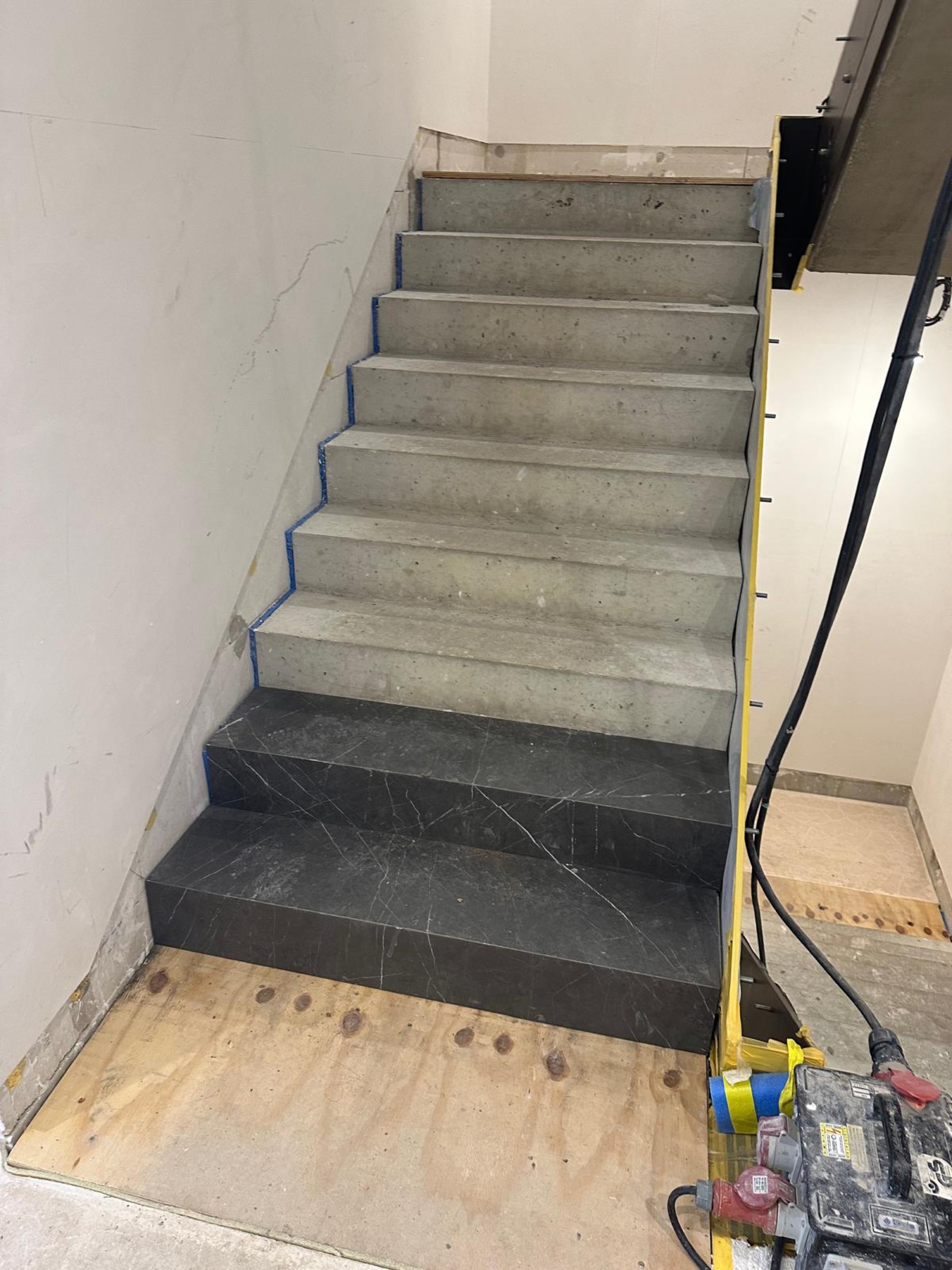 Treppe im Umbau: fertige Stufen aus schwarzem Marmor neben unverkleideten Rohbaustufen