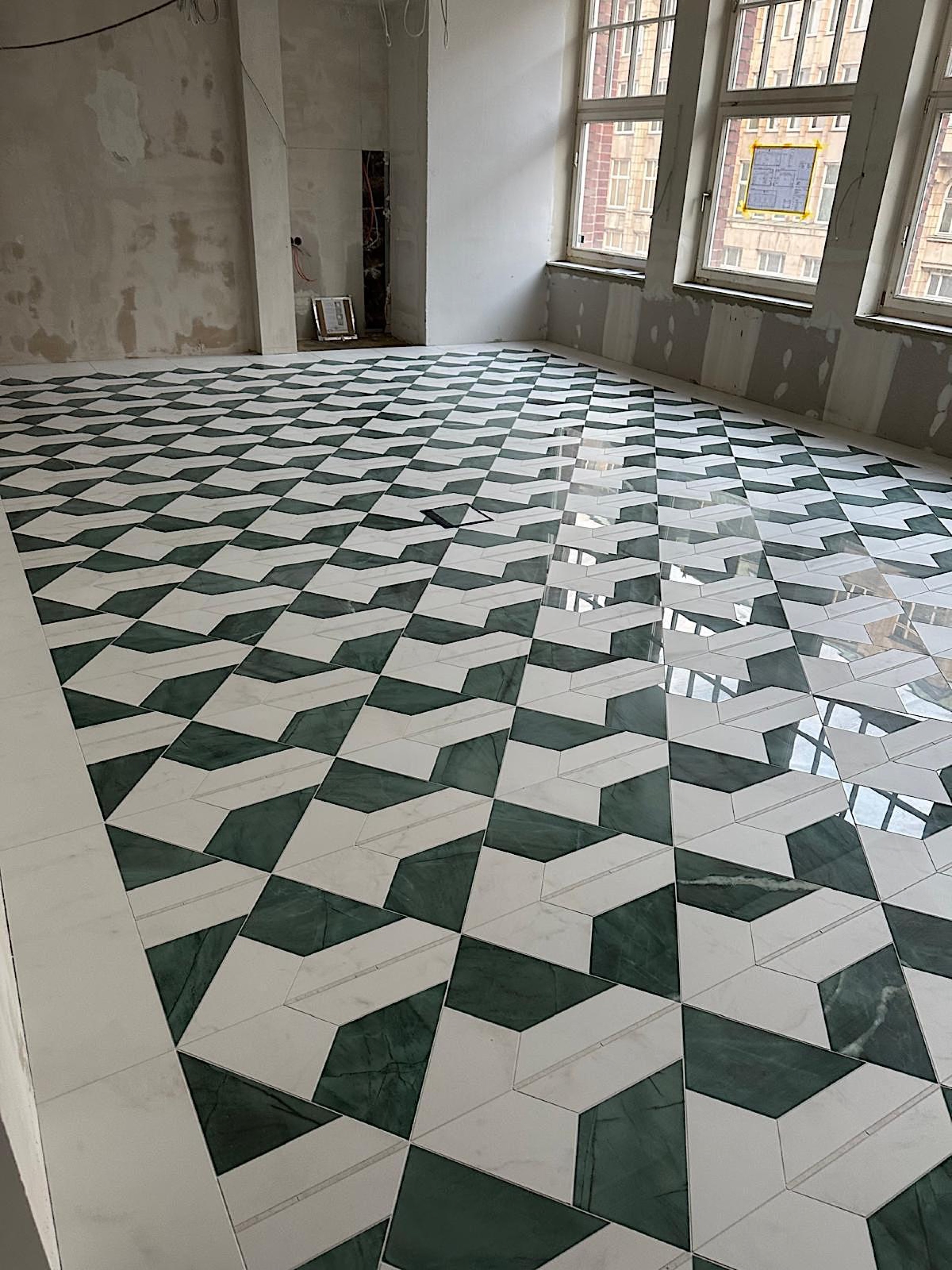 camt-verlegter-boden-mit-gruen-weissem-kubusmuster-im-rohbauraum-mit-hohen-fenstern-rechts-und-glaenzenden-spiegelungen