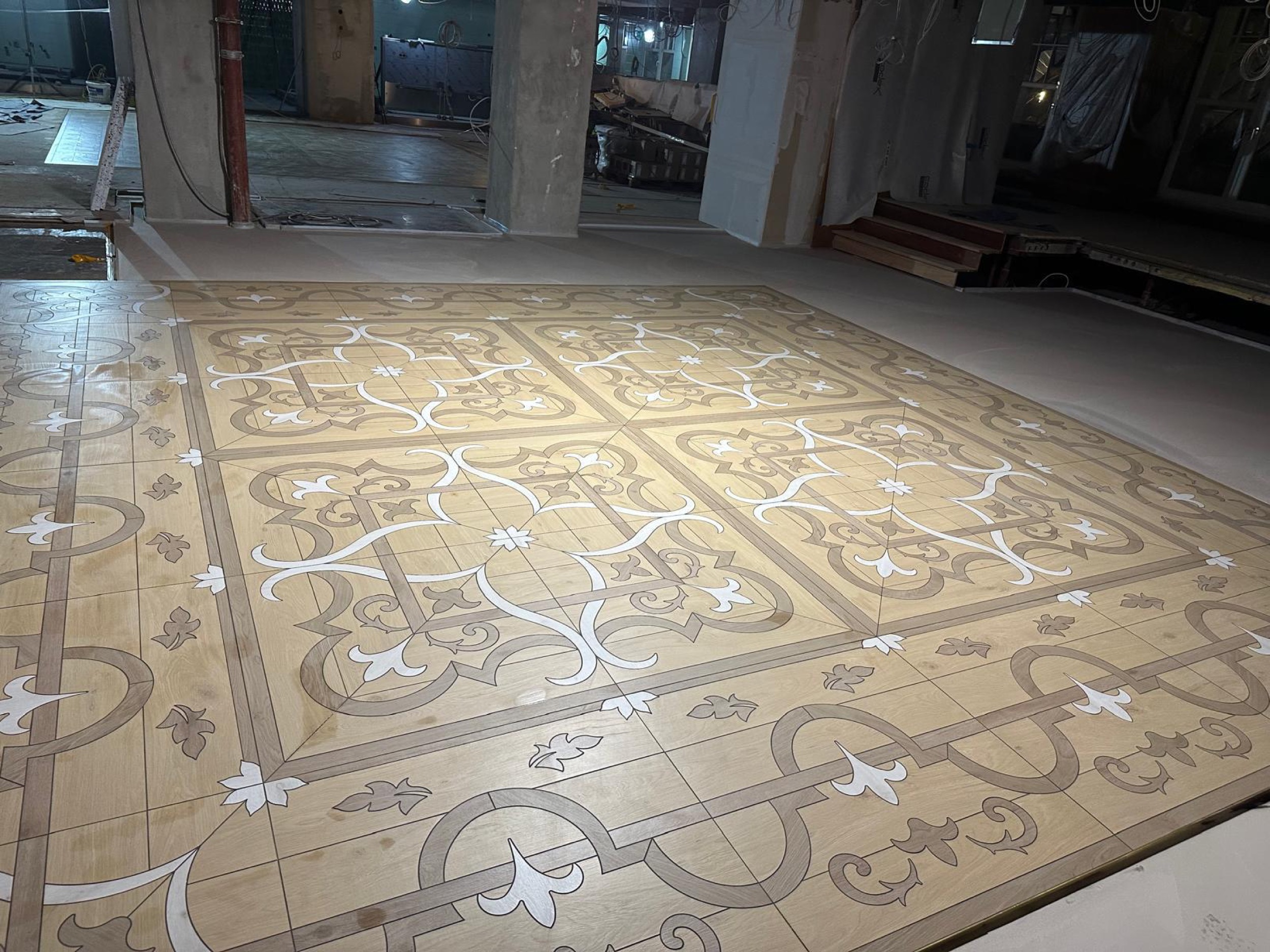 camt verlegter ornamentboden in holzoptik von der seite mit betonpfeilern und baustelle im hintergrund bei kuehlem licht