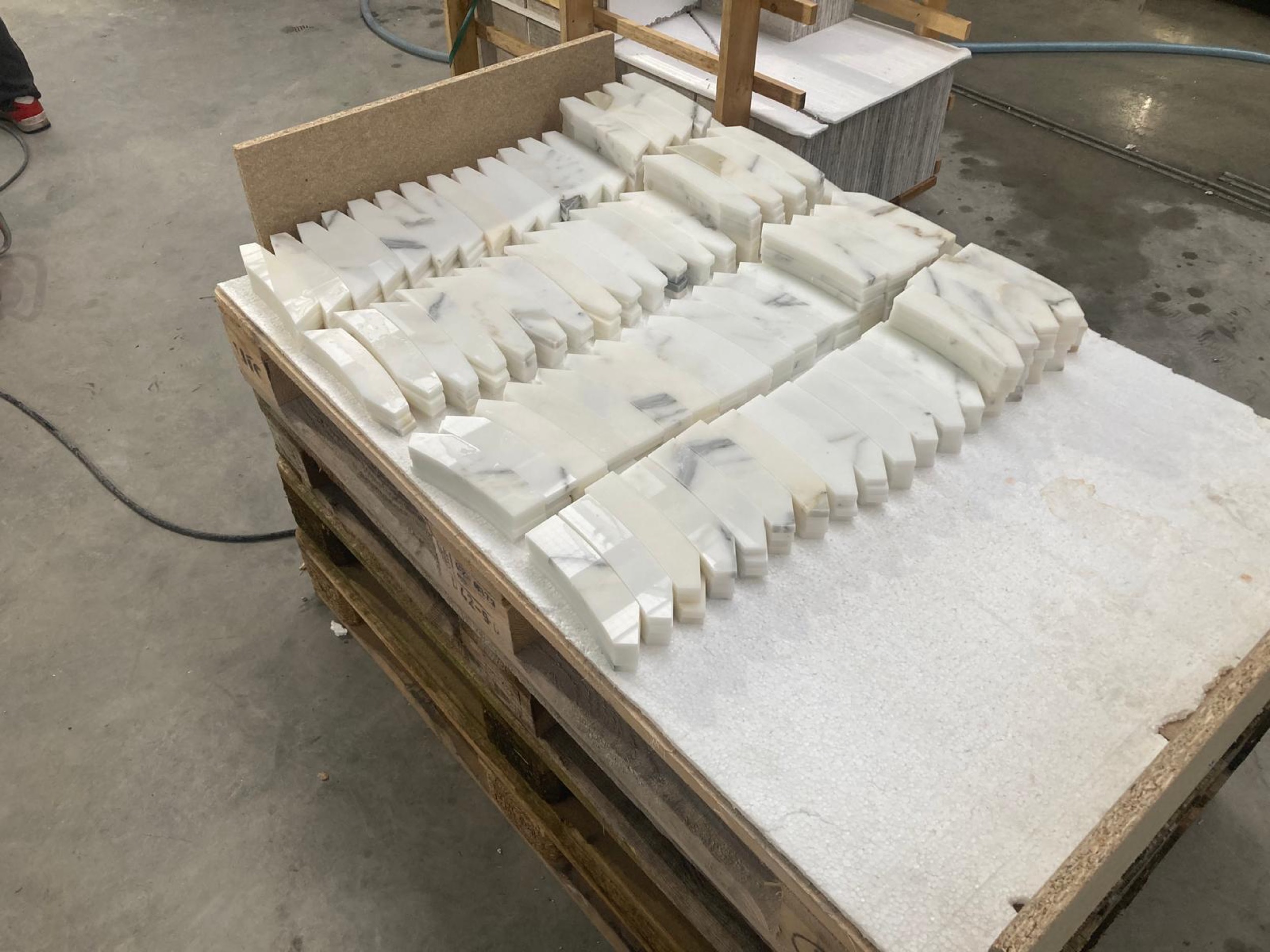 camt zugeschnittene weisse marmorteile mit grauen adern in gebogenen und gezackten formen auf einer holzpalette in der werkstatt